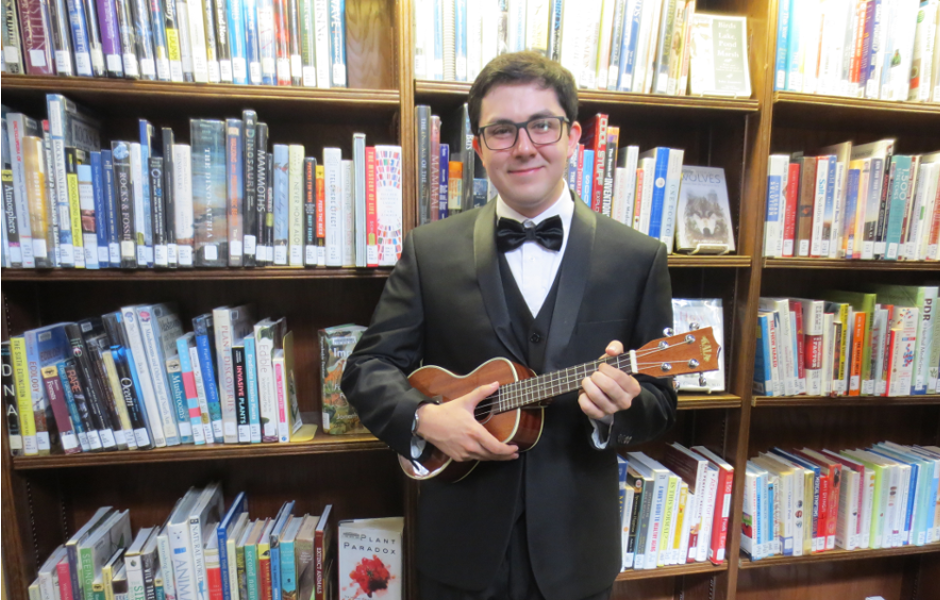 young man in a tux holding a ukulele in front of bookshelves